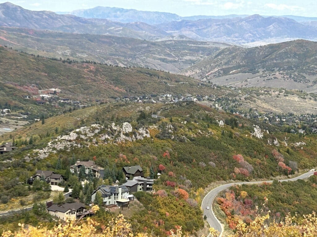 Fall colors on the hillsides above Deer Valley East Village homes and a winding mountain road near Park City, Utah