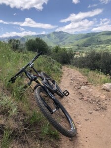 Mountain bike resting on a Park City singletrack trail with green hills behind